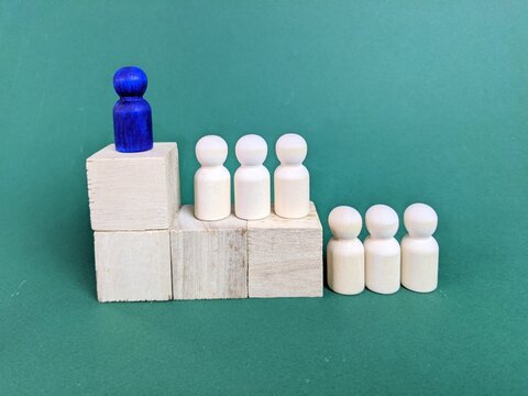 Wooden peg dolls on staircase blocks, with blue figure at top symbolizing leadership, hierarchy and progression.