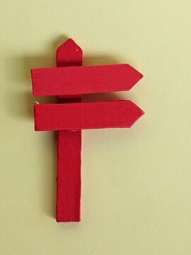 Red directional signpost made from craft materials, symbolizing guidance, navigation and creative design on a plain yellow background