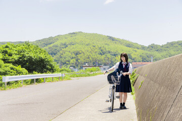 Fototapeta premium 海辺の通学路で自転車を押す女子高校生