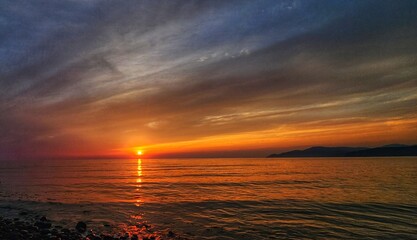 Naklejka premium Vivid orange sunset over the ocean with distant mountains on the horizon
