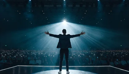 Male Public Speaker Standing on Stage with Arms Wide Open Facing Massive Audience with Spotlight Halo and Volumetric Light Rays at Large Conference Event © RisanRisan