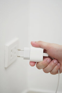 close up hand plugging adapter charge the battery with outlet socket plug and hold mobile phone on wall ,electric safety concept