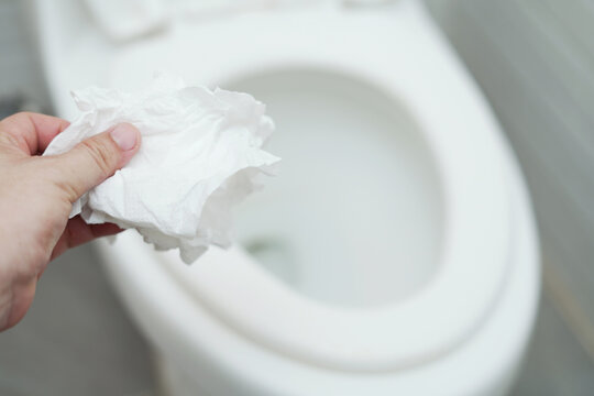 close up hand holding a tissue to be thrown into the toilet bowl. Can not drain water of toilet paper in the toilet bowl cause the stool to clog up.	