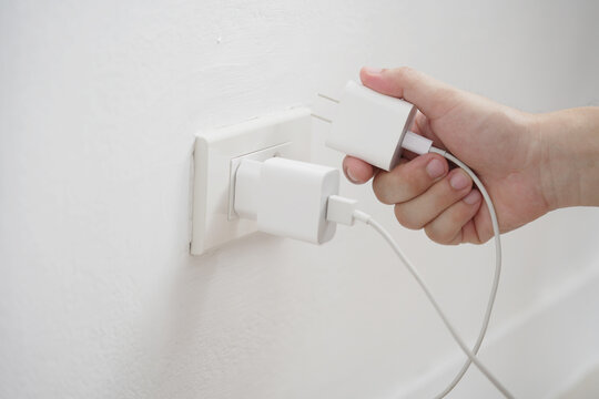 close up hand plugging adapter charge the battery with outlet socket plug and hold mobile phone on wall ,electric safety concept