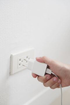 close up hand plugging adapter charge the battery with outlet socket plug and hold mobile phone on wall ,electric safety concept