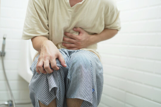 portrait of a man suffers from diarrhea his stomach painful. ache and problem. of toilet bowl. constipation in bathroom. Hygiene, health care concept.