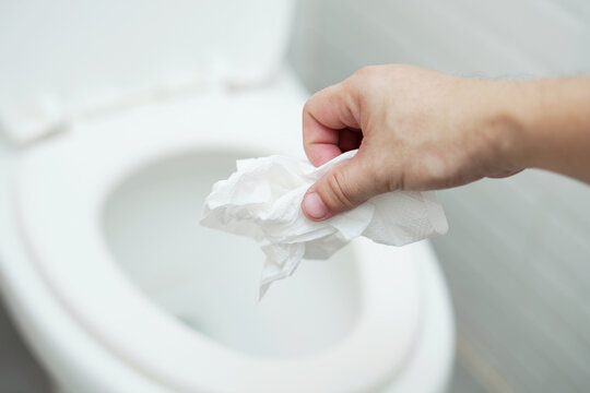 close up hand holding a tissue to be thrown into the toilet bowl. Can not drain water of toilet paper in the toilet bowl cause the stool to clog up.	