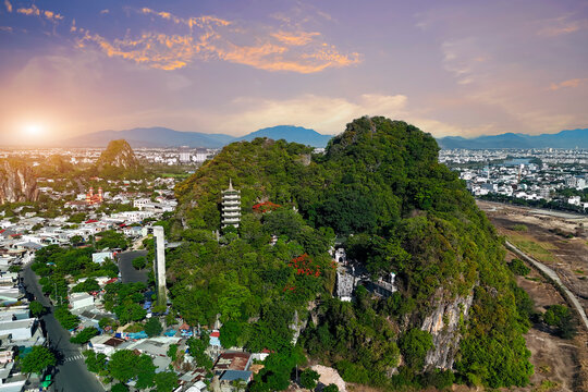 Marble mountains and rocks with a tower and a Buddhist style prayer temple overgrown with dense tropical vegetation against the backdrop of a beautiful lilac colored evening sky, view from above