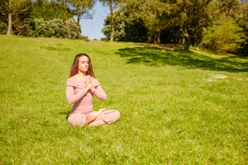 Fotobehang Lotusbloem Woman meditating in lotus pose on green grass  © Digito  Pitoresco