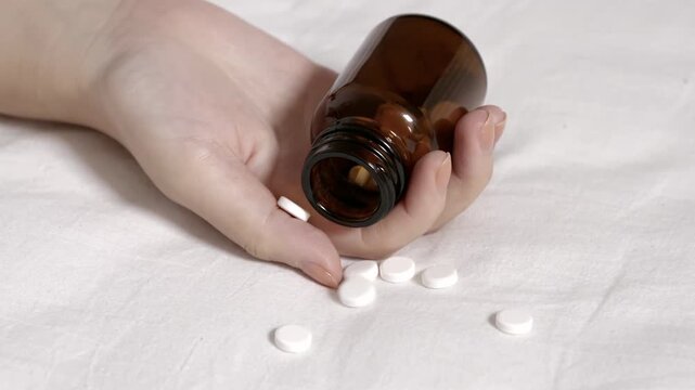 Unrecognized despair depressed young woman hand falls due to drug overdose with pill bottle and pills on the floor, unconscious boring female lying on bed after overdosing antidepressant medicine