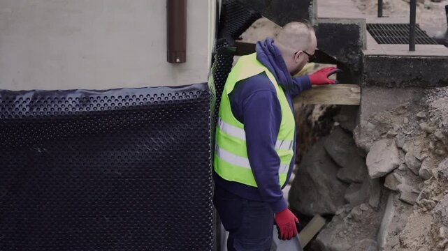 Construction inspector examines a dangerous excavation site wearing safety vest and gloves, useful for workplace safety, engineering, and site inspection concepts.
