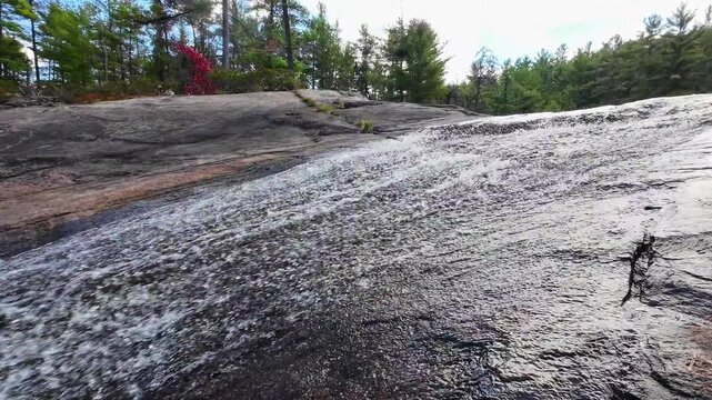 Upward view of High Falls flowing over a broad rock ledge in Algonquin Provincial Park, Ontario, Canada.