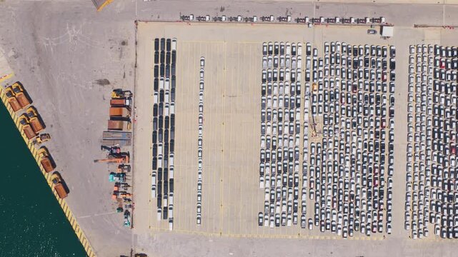 Hundreds of new cars parked in neat rows at a large automotive port terminal, waiting for loading and shipping to dealers and distributors in a global logistics and trade operation
