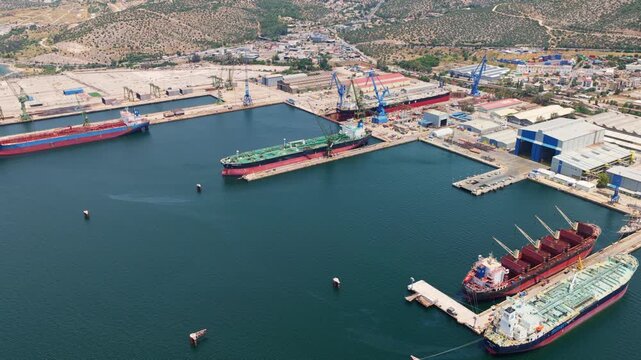 Expansive aerial view showcasing a large industrial port with massive cargo ships and tankers moored in the shipyard for maintenance and repair, with cranes and dry docks visible in the background