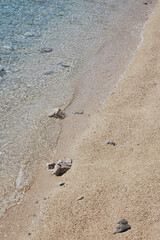 Obraz premium A high angle view of clear turquoise sea water gently washing onto a clean golden sand and pebble beach during a bright sunny day.