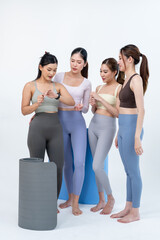 Obraz premium Asian women friends stand together beside rolled yoga mats, discussing wellness plan in minimal studio, trainer shares guidance for flexibility goals, posture balance, healthy fitness routine