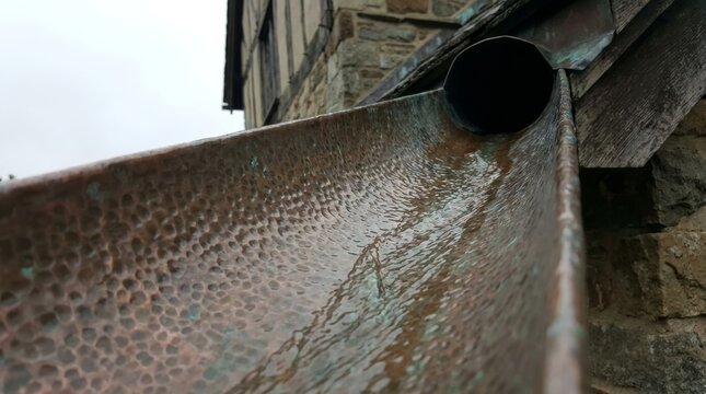 Detailed view of aged copper gutter with water flow and beautiful natural patina on stone facade