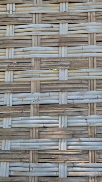 Low angle panning shot of a traditional hut corner with woven bamboo walls and corrugated zinc roof against a clear blue sky