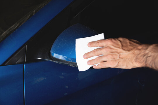 Man cleaning blue car mirror.