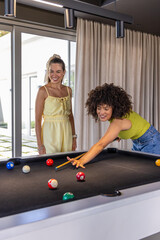 Naklejka premium Diverse female friends leaning and shooting cue at black-felt pool table, wearing colorful clothes