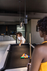 Naklejka premium Diverse female friends playing pool in modern game room with black felt table, racked balls, cues