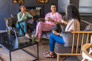 Obraz premium Diverse female friends recording on boom mics in living room, sipping green drinks in lounge wear