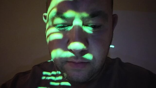 Computer hacker working in dark room with green programming code projected on his face, cyber security concept