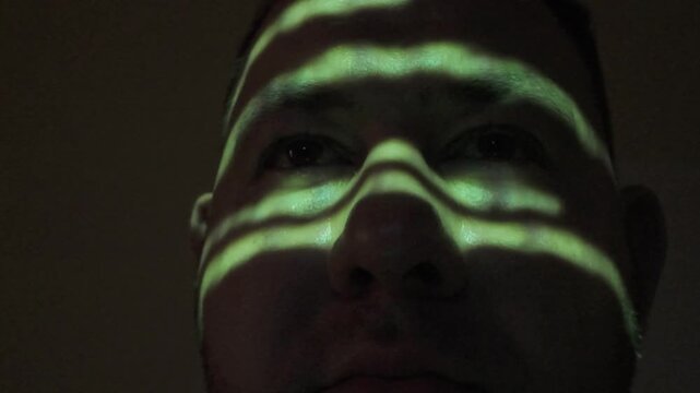 Computer hacker working in dark room with green programming code projected on his face, cyber security concept