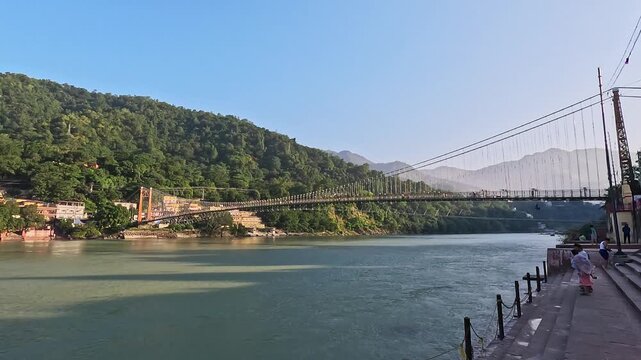 Beautiful landscape of Ram Jhula suspension bridge, holy Ganga River, and concrete bathing ghats in Rishikesh