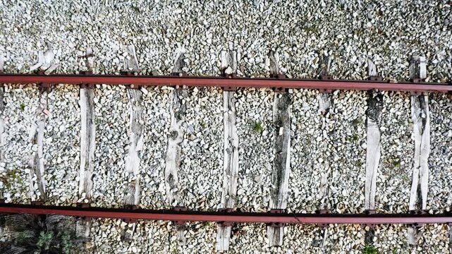 Drone view moving over old rusty train tracks with weathered wooden sleepers on gravel bed