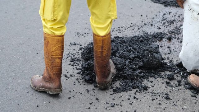 road worker boots standing beside fresh asphalt during street repair, paving, and road maintenance work.