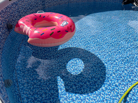 Pink donut floatie casting shadow in swimming pool