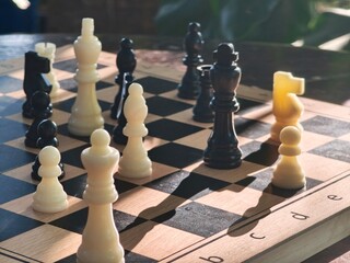 A close-up shot of a chess game in progress on a wooden board under warm sunlight, casting long shadows © Housewife Stocker
