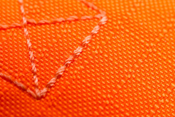 Fototapeta premium Orange fabric texture with visible stitching, close up of textile surface showing detailed thread pattern and geometric design, vibrant color, macro photography