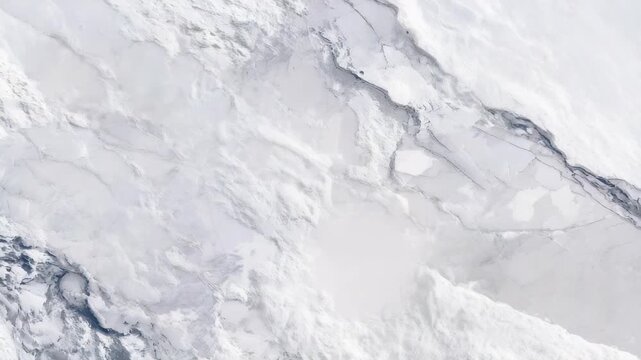 Aerial view of a vast frozen landscape covered in white snow and ice, showcasing natural patterns and textures. The abstract winter scene evokes a sense of cold, isolation, and tranquility