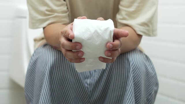 portrait of a man suffers from diarrhea his stomach painful. ache and problem. hand hold tissue paper roll in front of toilet bowl. constipation in bathroom. Hygiene, health care concept.	
