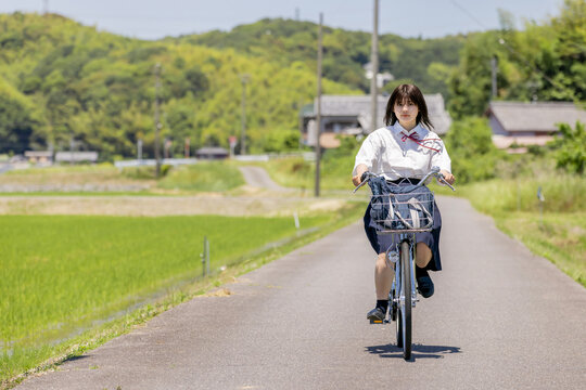 田園風景の通学路を自転車で走る女子高校生