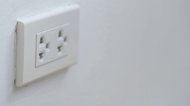 close up hand plugging adapter charge the battery with outlet socket plug and hold mobile phone on wall ,electric safety concept