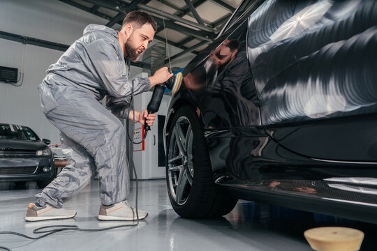 Worker polishing car with special grinder and wax from scratches at the car service station. Professional car detailing and maintenance concept