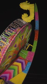 Colorful mela jhula ride at night, Neon illuminated carnival thrill ride, Amusement fair ride under dark sky, Bright fairground swing attraction closeup stock video.