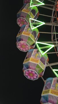 Ferris wheel cabins glowing at night fair, Colorful mela jhula gondolas under dark sky, Neon lit carnival wheel close up, Amusement ride cabins at festive fair stock video.