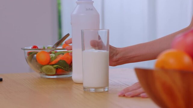 Milk Glass Bottle Hand Vegetable Fruit Kitchen Table Breakfast Nutrition Pouring Fresh Milk Into Clear Glass Beside Salad Bowl Fruit On Wooden Surface