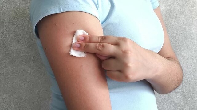 Woman applying cotton pad to arm after vaccination, immunization procedure, healthcare and medical prevention concept.