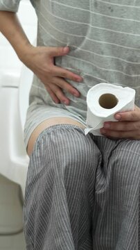 portrait of a man suffers from diarrhea his stomach painful. ache and problem. hand hold tissue paper roll in front of toilet bowl. constipation in bathroom. Hygiene, health care concept.