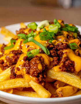 Appetizing chili cheese fries loaded with rich seasoned chili, golden crispy french fries in creamy melted cheddar cheese sauce, sliced green onions, tasty food. Close-up.