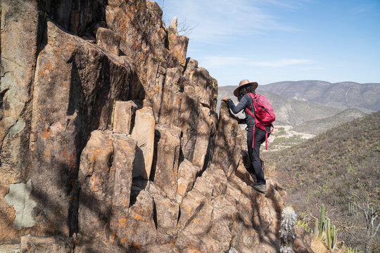 Woman in a hat scrambles up a rocky cliff face