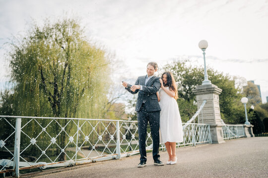 Happy couple celebrating engagement with champagne spray in park