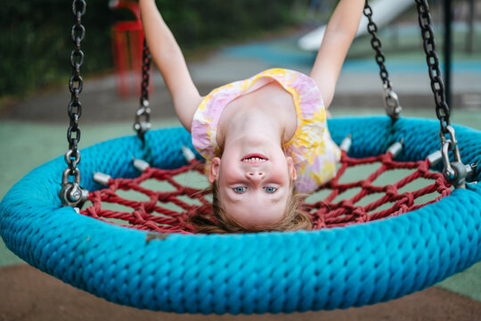 Happy little girl hanging upside down on playground swing
