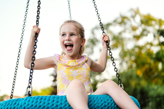 Happy little girl playing on rope swing at playground