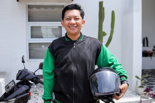 Portrait of Smiling Young Indonesian Online Motorcycle taxi Driver Standing Outdoors
